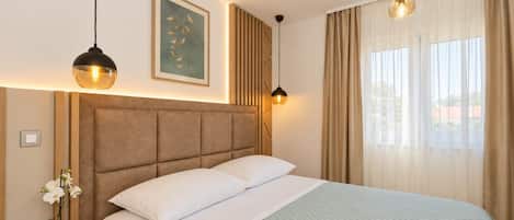 Bright double bedroom with upholstered headboard, modern bedside lighting, soft bedding, and elegant neutral decor.