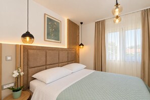 Habitación de hotel con una cama grande, cabecera, un cuadro en la pared, planta en maceta y ventana con cortinas.
