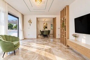 Una sala moderna con un sofá verde, un comedor con mesa y sillas, un televisor montado en la pared y un ventanal con cortinas.