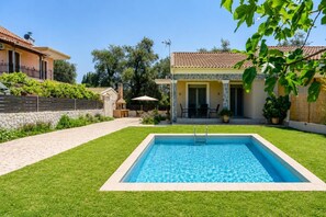 A swimming pool surrounded by a well-maintained lawn, with a patio area and a stone wall in the background. - Villa Boltado - Two Bedroom Villa, Sleeps 4 (Lefkimmi)