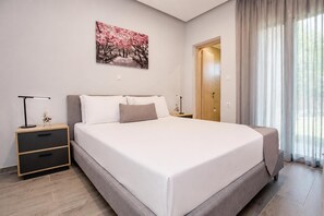 Ein modernes Schlafzimmer mit einem großen Bett, einem Nachttisch mit Schubladen, einem Beistelltisch, einer Tür und einem Fenster mit Vorhängen.