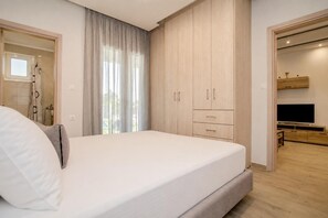 A bedroom with a bed, a wardrobe, a television, and a bathroom visible through an open door. - Villa Boltado - Two Bedroom Villa, Sleeps 4 (Lefkimmi)