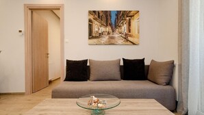 Ein Wohnzimmer mit einer Couch, einem Glastisch mit Dekoration und einem Wandbild einer Straßenszene.