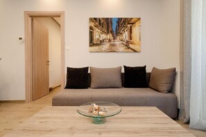A living room with a sofa, a glass coffee table with decorative items, and a wall-mounted picture of a street scene. - Villa Boltado - Two Bedroom Villa, Sleeps 4 (Lefkimmi)