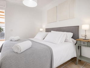 A neatly made bed with white linens and a grey blanket, a bedside table with a lamp, and a view of the outside balcony. - Villa Anaiaks - Five Bedroom Villa, Sleeps 9 (Caleta de Fustes)