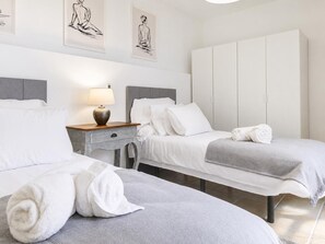 Ein Hotelzimmer mit zwei Betten, einem Nachttisch mit Lampe, einem Kleiderschrank und einem Kunstwerk an der Wand.