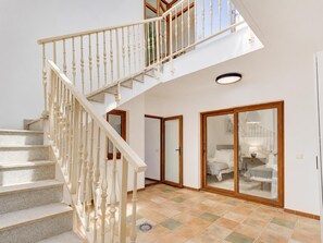 A staircase with a white balustrade leading to a second floor, a glass door with a bed visible inside, and a tiled floor. - Villa Anaiaks - Five Bedroom Villa, Sleeps 9 (Caleta de Fustes)