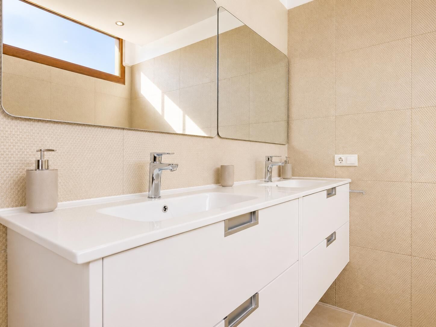 A modern bathroom with two sinks, a large mirror, and a window.