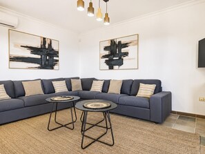 A modern living room with a dark blue sectional sofa, two round tables, and abstract paintings on the walls. - Villa Anaiaks - Five Bedroom Villa, Sleeps 9 (Caleta de Fustes)