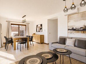 Ein modernes Wohnzimmer mit Sofa, Couchtisch, Esstisch, Stühlen und Pendelleuchten.