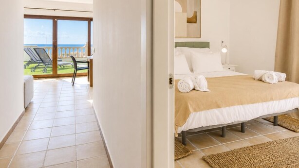 Quarto de hotel com uma cama, vista para o mar, varanda com cadeiras e ar condicionado.