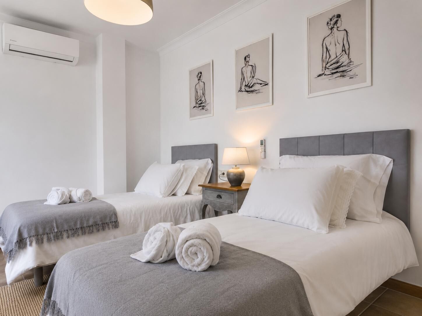 A hotel room with two beds, a bedside table with a lamp, and three wall-mounted artworks.