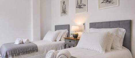 A hotel room with two beds, a bedside table with a lamp, and three wall-mounted artworks.