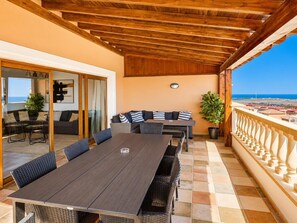 Une terrasse extérieure couverte, aménagée avec une table et des chaises, un canapé et un pot de fleurs.