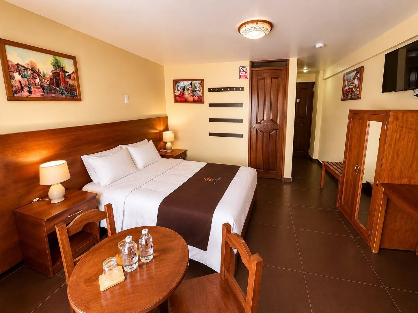 Ein Hotelzimmer mit einem großen Bett, Nachttischen mit Lampen, einem Holztisch mit Stühlen und Kunstwerken an den Wänden.