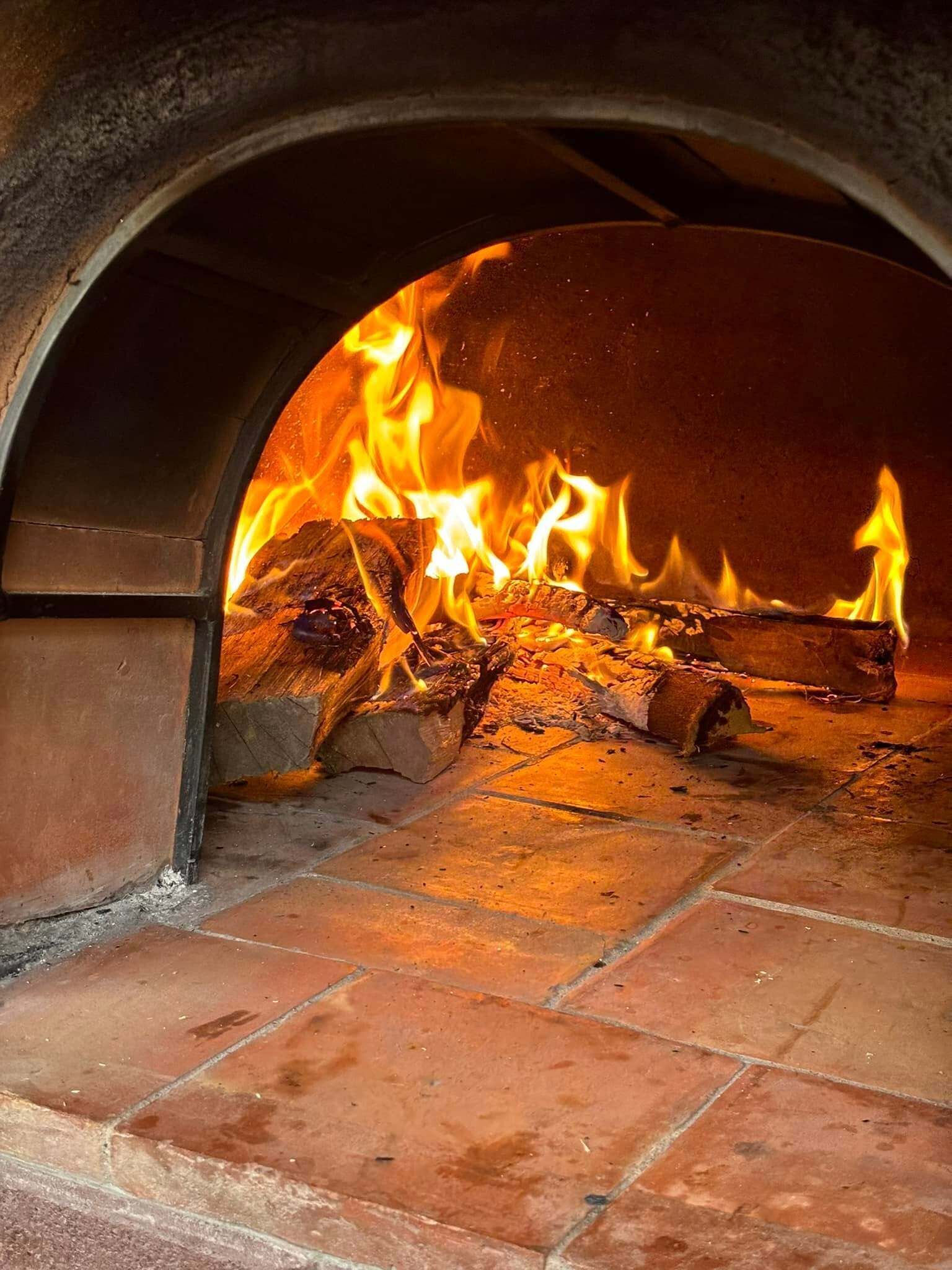 Horno de ladrillo con fuego encendido en su interior, indicando un lugar para cocinar o hornear.