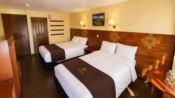 Habitación de hotel con dos camas, cabecera de madera, mesita de noche, escritorio y lámpara de pared.