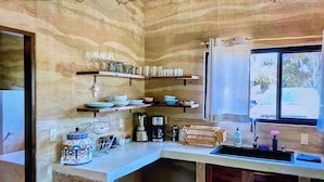Eine Küche mit Steinwand, Regalen mit Geschirr, einer Kaffeemaschine und einem Spülbecken.