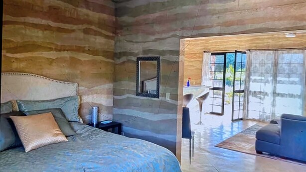 Ein Schlafzimmer mit Bett, Nachttisch, Spiegel und Blick ins Freie durch eine Tür.