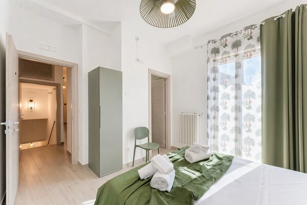 A hotel room with a bed, a chair, a radiator, and a view of the outdoors.