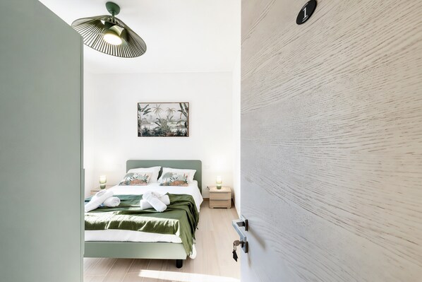 A bedroom with a bed, bedside lamps, a wall-mounted artwork, and a door with a number plate.