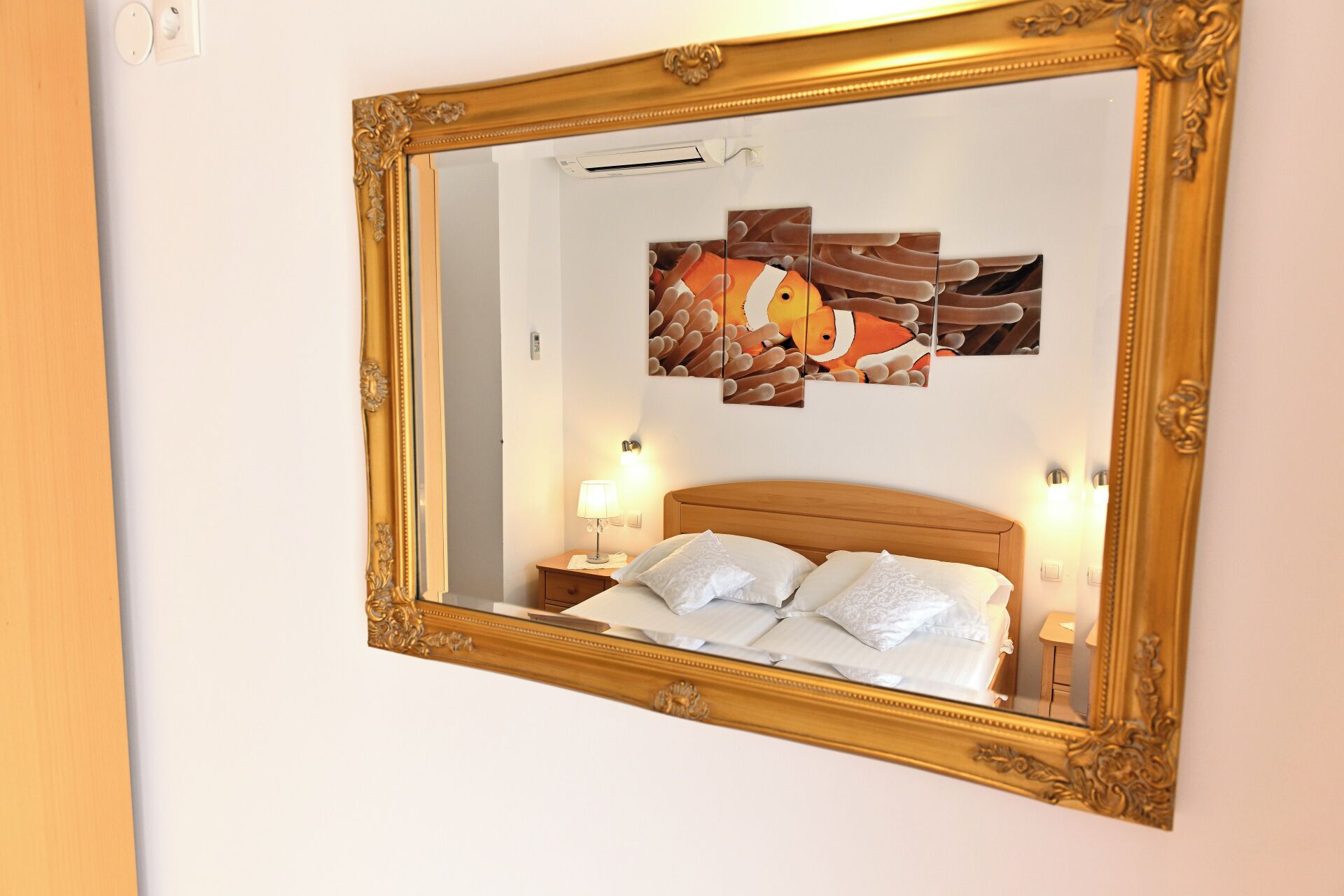 Ein Schlafzimmer mit einem großen, verzierten Spiegel, einem Bett mit weißen Bettwäsche und einem an der Wand hängenden Kunstwerk.