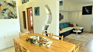 Een eetgedeelte met een houten tafel gedekt voor een maaltijd, een woonkamer met een bank en een schilderij, en een gang met kunstwerken aan de muren.