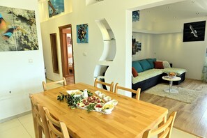Ein Essbereich mit Holztisch, gedeckt für eine Mahlzeit, ein Wohnzimmer mit Sofa und Gemälde sowie ein Flur mit Bildern an den Wänden.