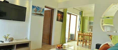 Una sala de estar moderna con un televisor de pantalla plana, muebles de madera, un comedor con una mesa verde y una cocina con microondas.