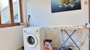 Een wasruimte met een wasmachine, een strijkplank en een stofzuiger.