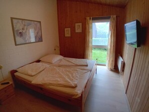 Ein Schlafzimmer mit einem hölzernen Bett, einem an der Wand befestigten Fernseher und einem Fenster mit Vorhängen.