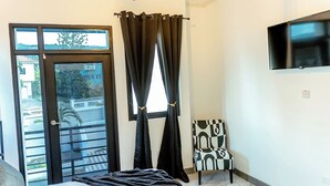 Ein Schlafzimmer mit Bett, Sessel, Fernseher und einem Fenster mit Vorhängen.