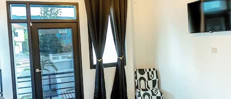 A bedroom with a bed, a chair, a TV, and a window with curtains.