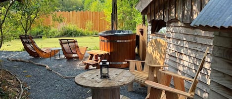 A wooden outdoor seating area with a hot tub, a table, and chairs.