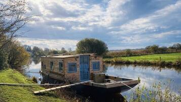 Een stilstliggende woonboot met een steiger, een klein dek en een deur.
