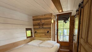 A wooden cabin bedroom with a bed, a small window, and a star decoration on the wall. - Unusual: A Tiny Hut in the Marais Region of Normandy (Liesville-sur-Douve)
