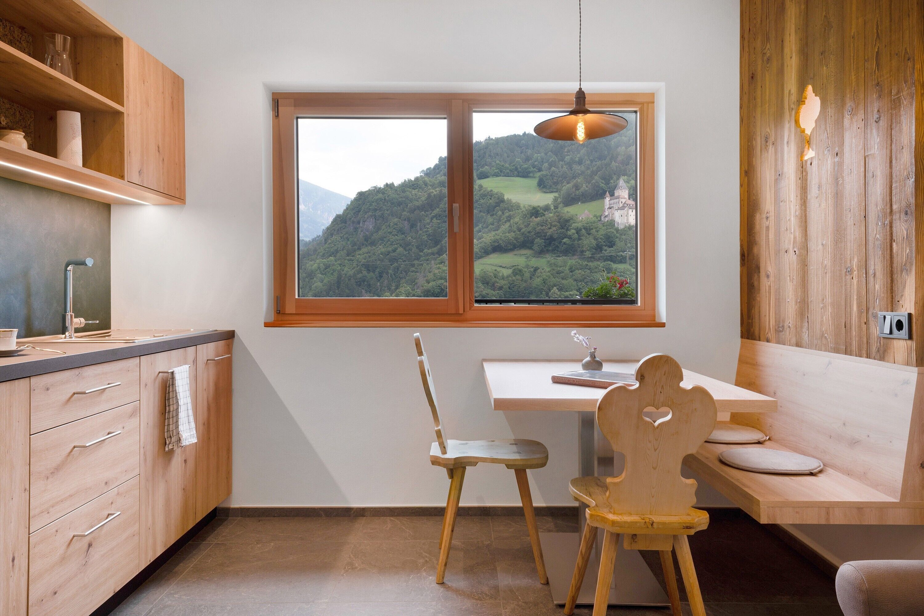 Een keuken met uitzicht op een kasteel, houten keukenkastjes, een eettafel met stoelen en een hanglamp.