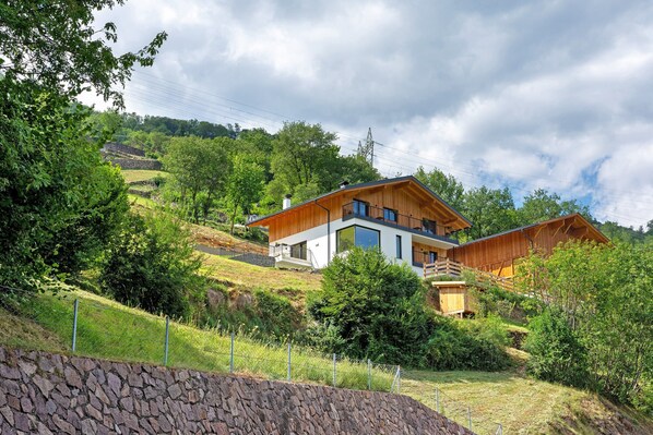 A modern two-story house with a stone retaining wall in the foreground, surrounded by lush greenery and hills. - Apartment 'Trostburg' with Mountain View and Wi-Fi (Barbian)