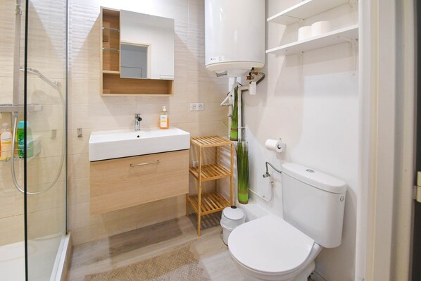 Et moderne badeværelse med en glasbrusekabine, en hvid vask, et toilet og en trækommode.