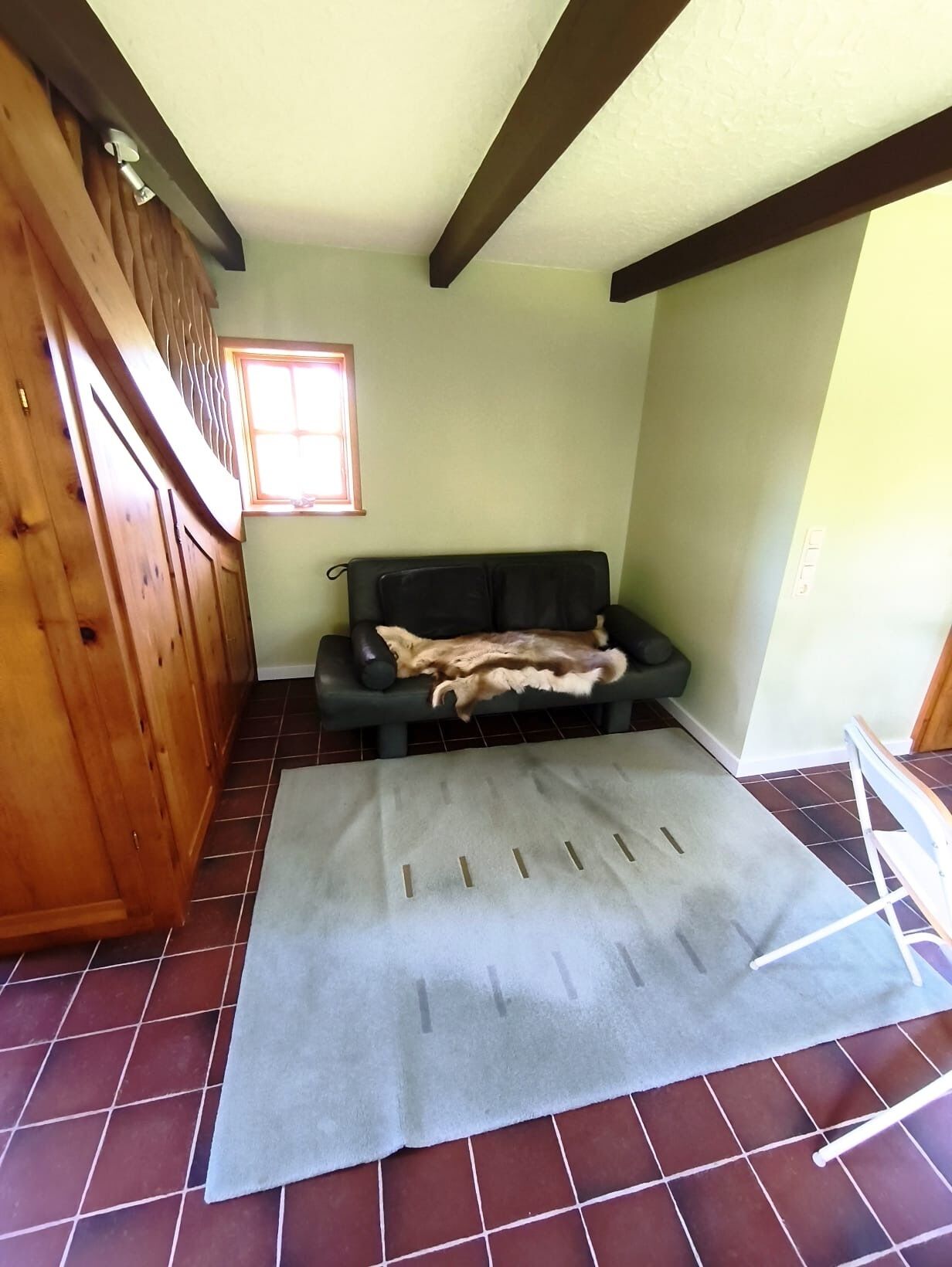 A room with a black leather sofa, a grey rug, wooden cabinets, and a window with natural light.