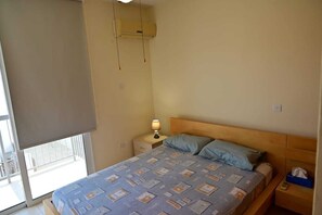 A bedroom with a bed, a nightstand, a lamp, and a window with a view.