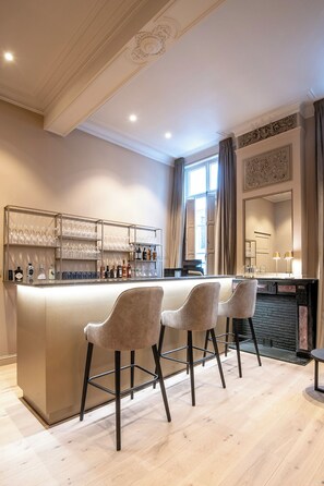 Una zona de bar con mostrador, taburetes y una vinoteca con botellas.