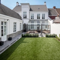 A courtyard with a glass conservatory, a lawn, and a seating area with tables and chairs.