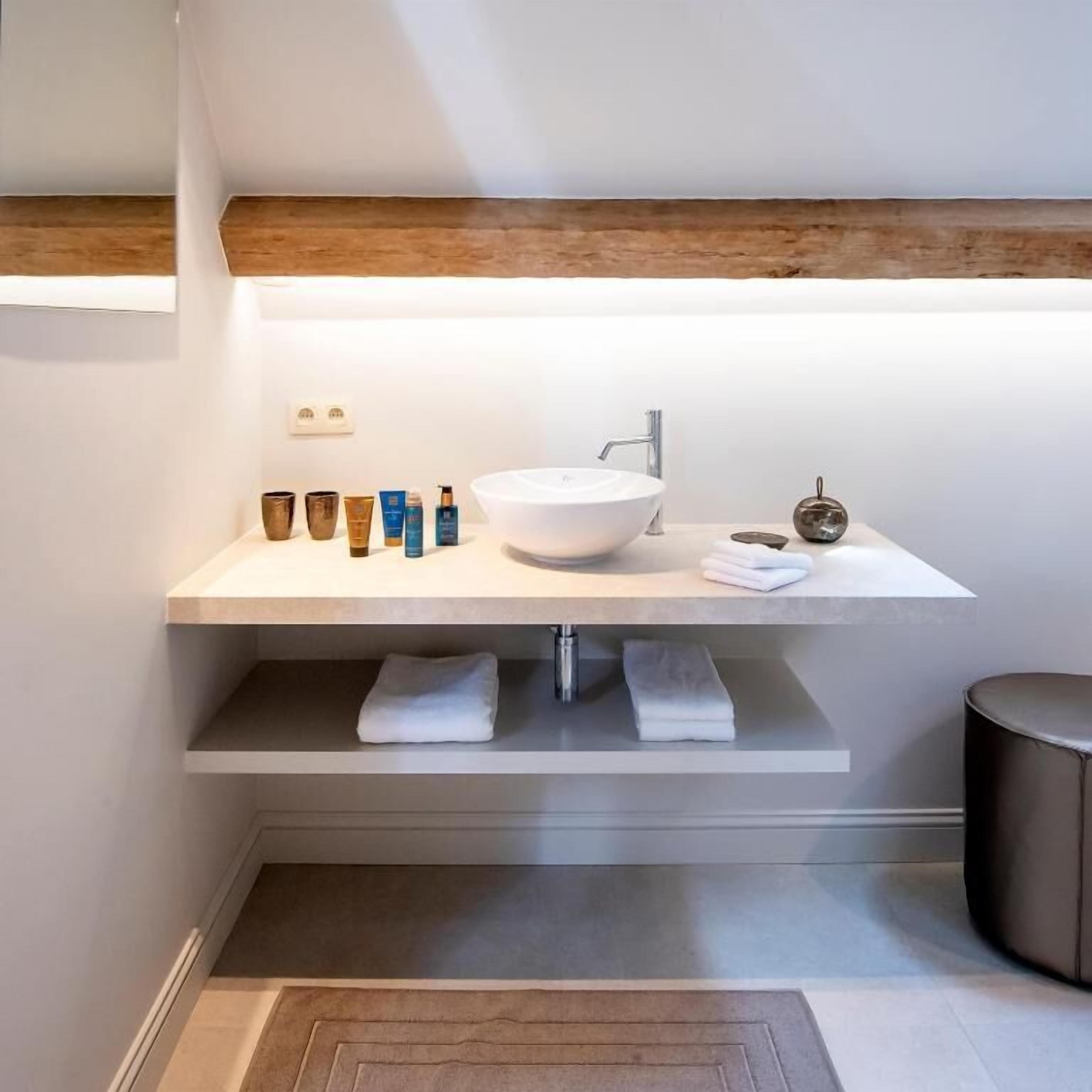 A modern bathroom with a large white sink, a mirror, and a shelf with toiletries.