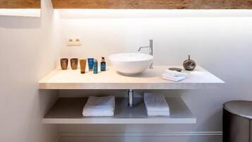 A modern bathroom with a large white sink, a mirror, and a shelf with toiletries.