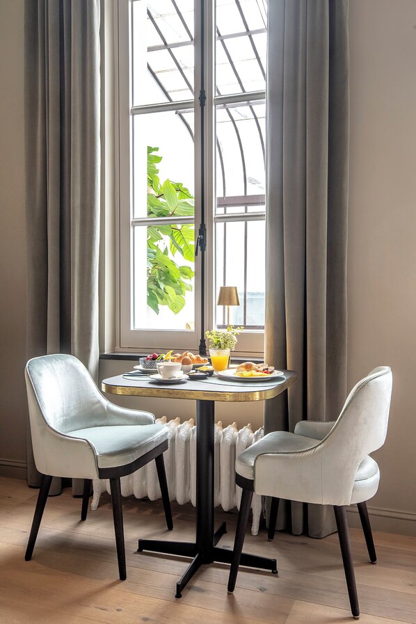 A dining area with a round table, two chairs, a lamp, and a window with curtains.