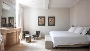 Un dormitorio con una cama grande, una chimenea, dos sillones y cuadros enmarcados en la pared.