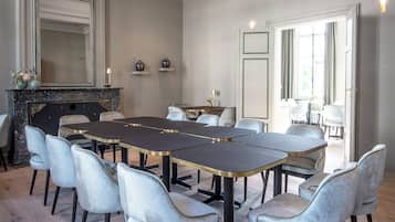 Een vergaderruimte met een lange rechthoekige tafel, omringd door stoelen, een open haard en een grote spiegel aan de muur.