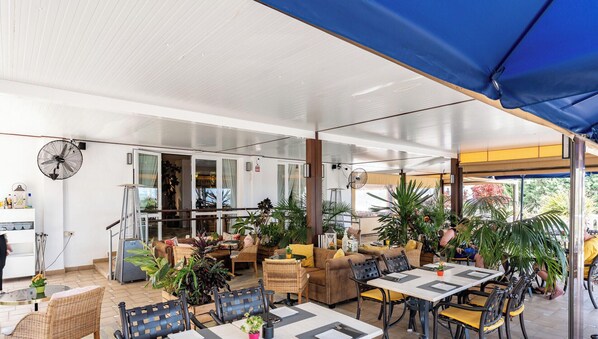 Ein Terrassenbereich im Freien mit Tischen, Stühlen, Blumentöpfen und einem Deckenventilator.