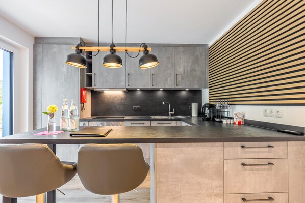 Une cuisine moderne dotée d’un îlot central, de luminaires suspendus et d’un four encastré.